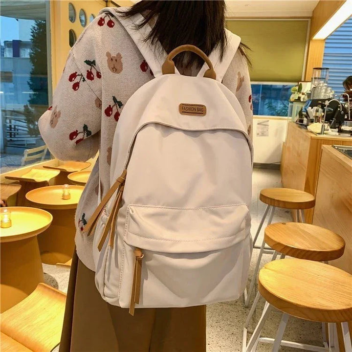 Woman wearing beige backpack with front pocket and leather zipper pulls in cozy cafe setting