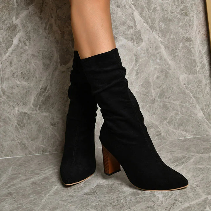 Black suede mid-calf boots with wooden stacked heels worn on marble floor background
