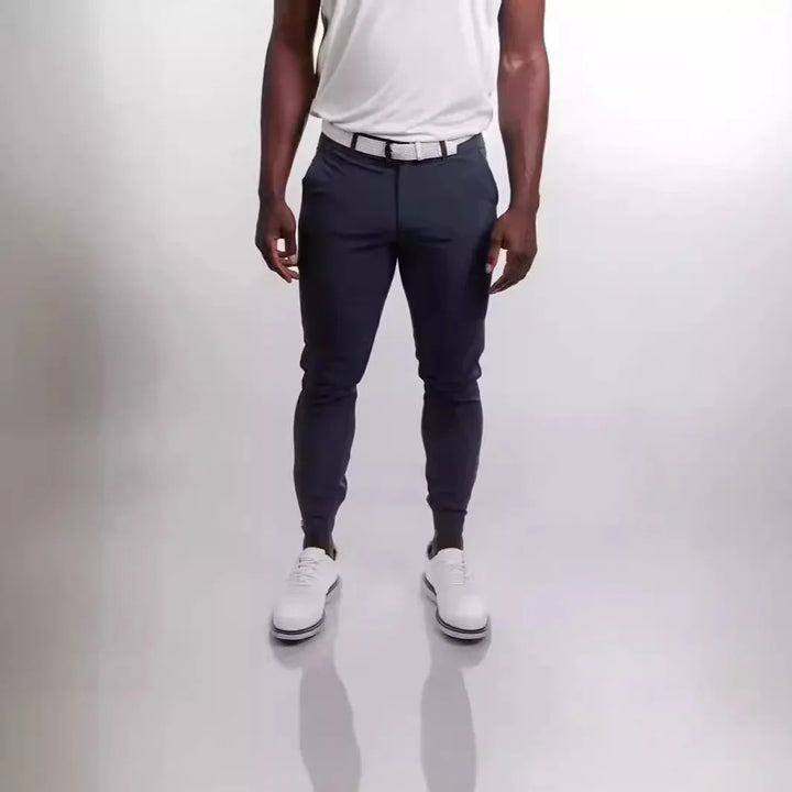 Man wearing dark slim-fit casual pants, white belt, white shirt, and white shoes on white background