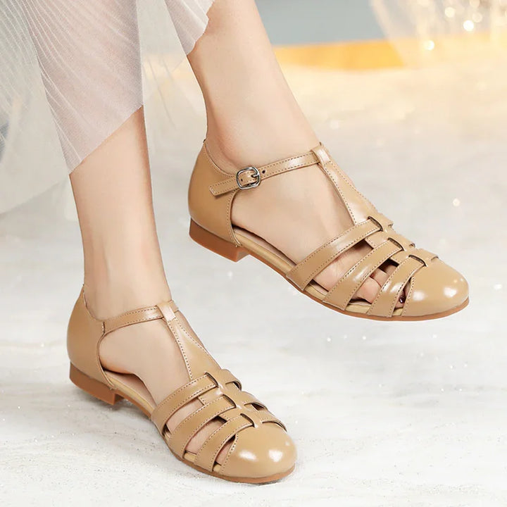 Womens beige leather flat sandals with ankle straps and cutout design, worn with sheer skirt