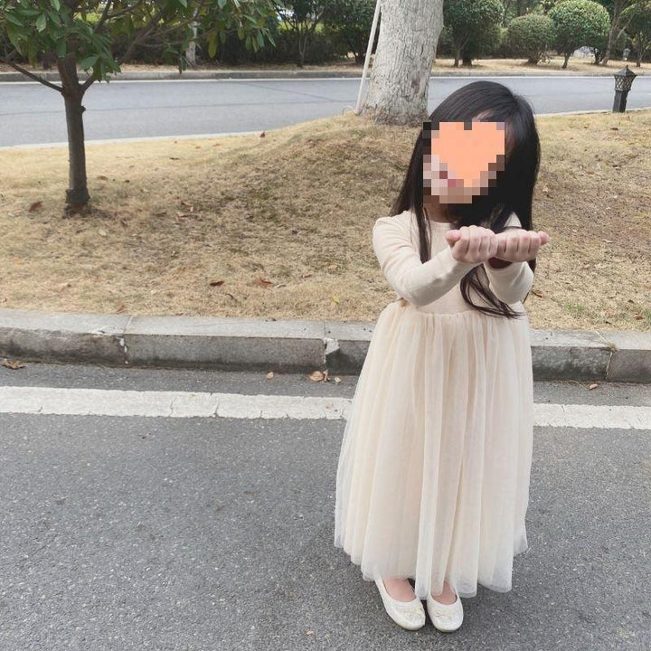 young girl in cream tulle dress and white shoes standing on pavement near grass and trees