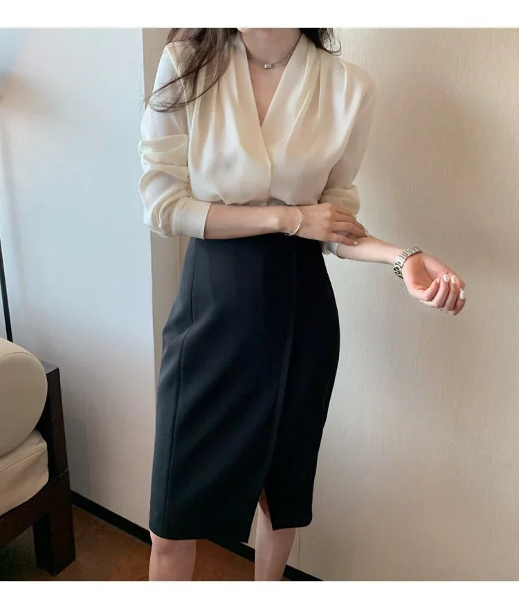 Woman wearing white blouse and black pencil skirt adjusting sleeve in minimalist indoor setting