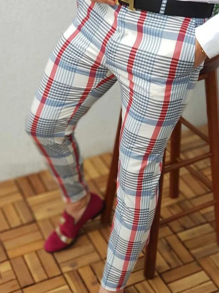 Person sitting on wooden chair wearing white plaid pants with red and blue stripes and red loafers