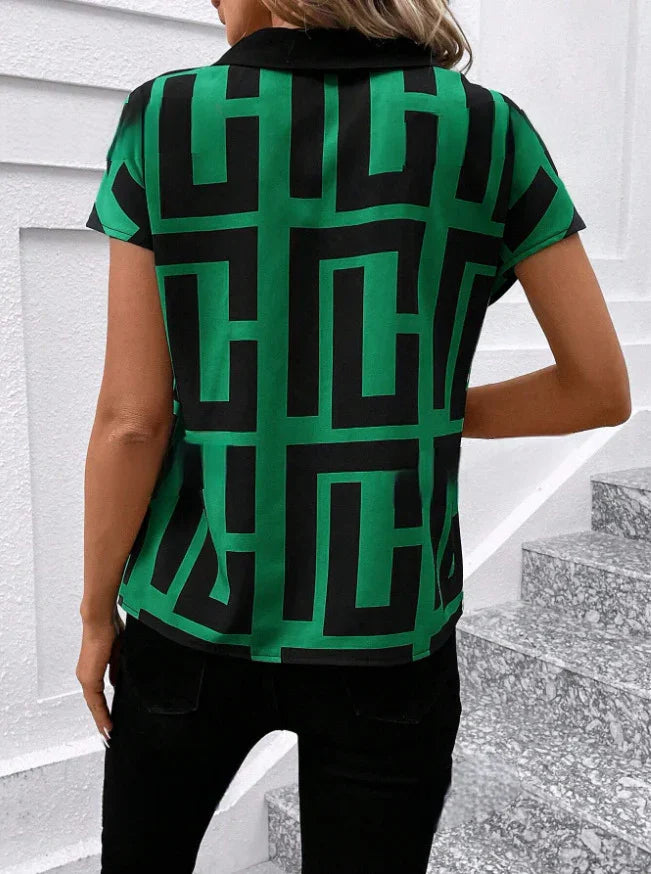 Woman wearing a green and black geometric patterned short-sleeve shirt with black pants on grey stone stairs