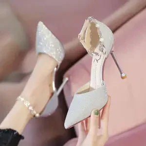 Elegant silver high heel shoes with pointed toes and ankle straps worn on feet against a pink background