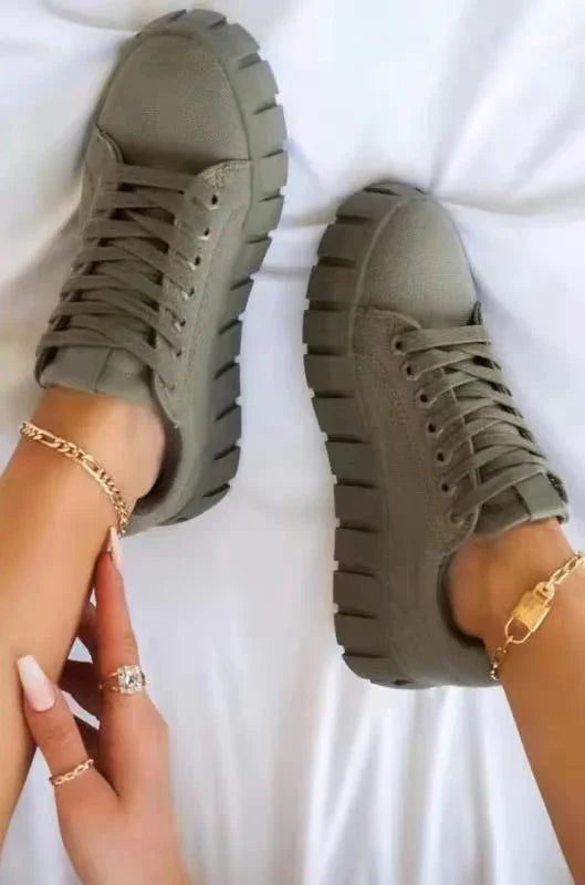 Pair of chunky olive green casual sneakers with thick soles worn on feet with gold anklets and rings