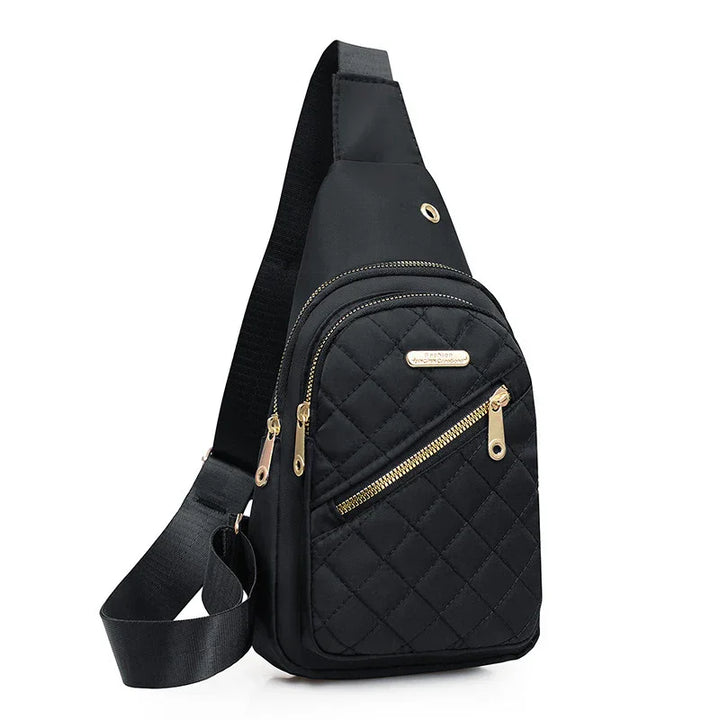Black quilted sling bag with gold zippers and adjustable strap on white background