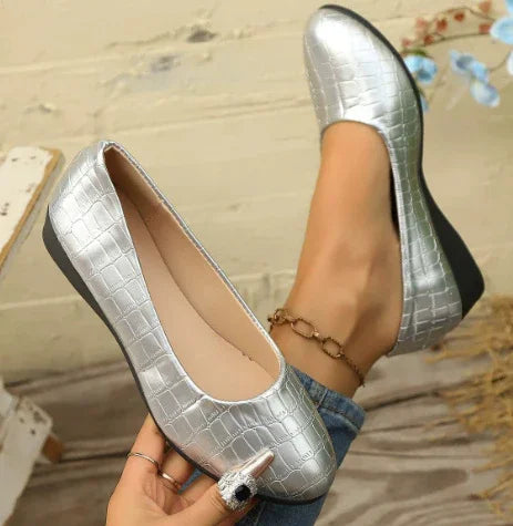 Woman wearing metallic silver croc-embossed wedge shoes with beige interior and ankle bracelet