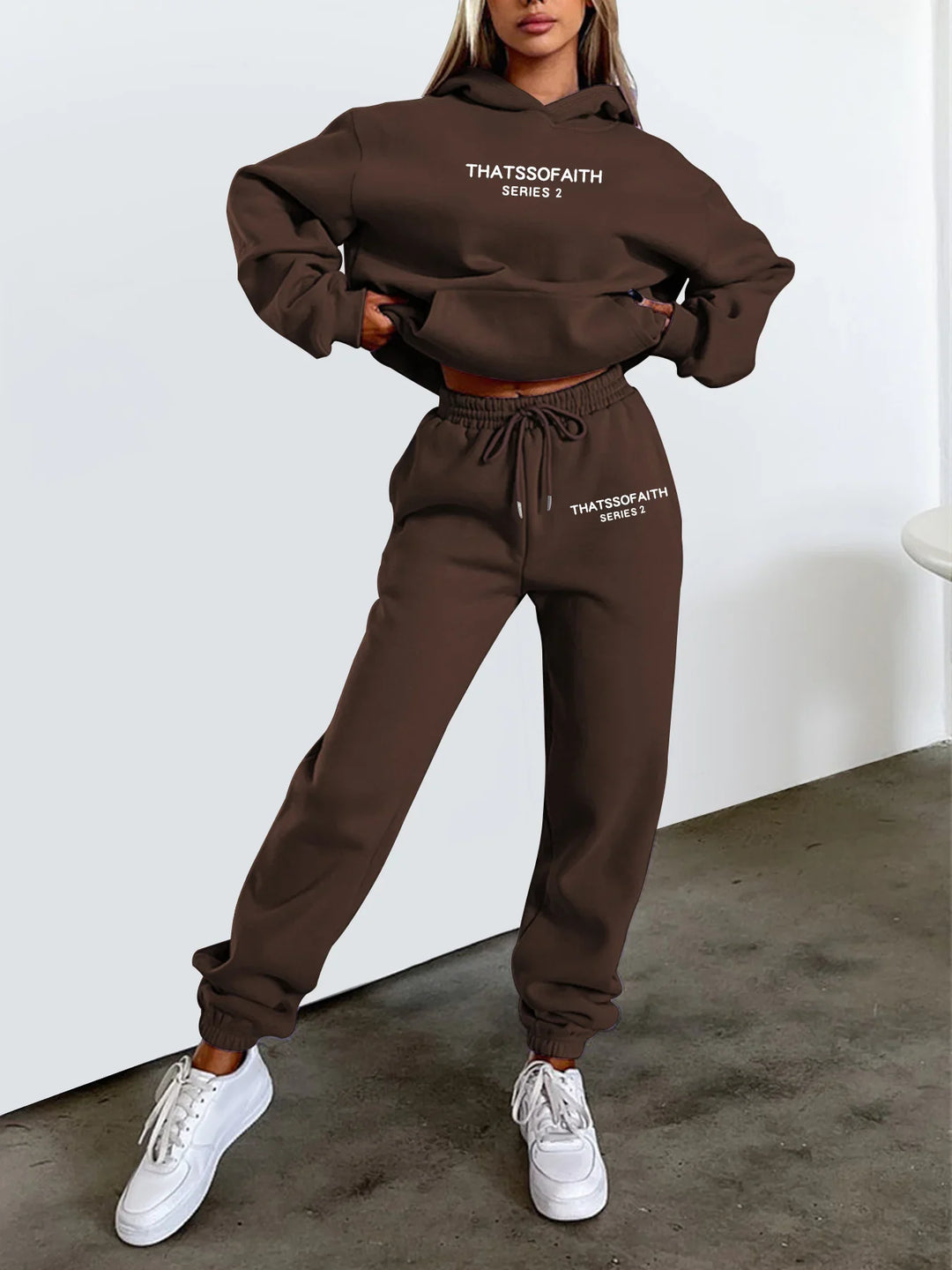 Woman modeling brown sweatshirt and joggers set with white text THATSSOFAITH SERIES 2, wearing white sneakers indoors
