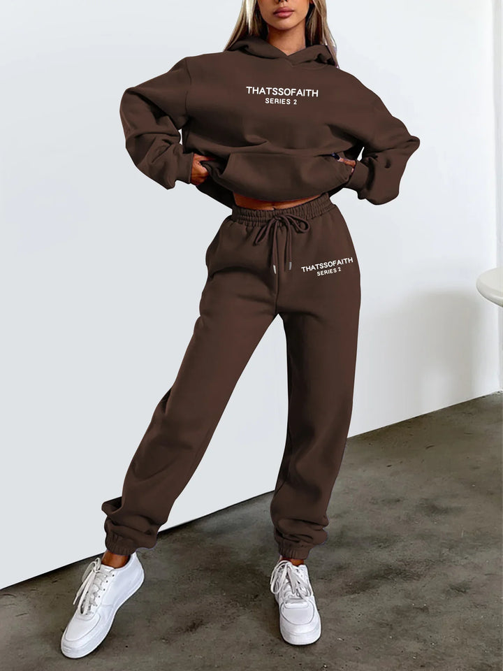 Woman modeling brown sweatshirt and joggers set with white text THATSSOFAITH SERIES 2, wearing white sneakers indoors