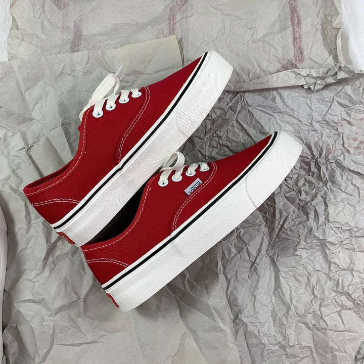 Pair of red canvas Vans sneakers with white laces and thick white soles on crumpled paper