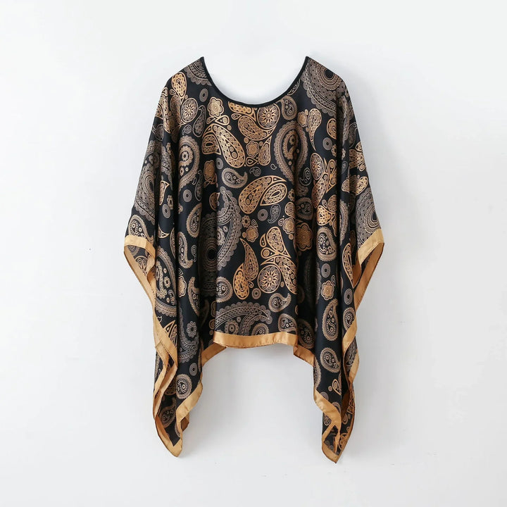 Black and gold paisley patterned loose top with golden trim hanging on white wall