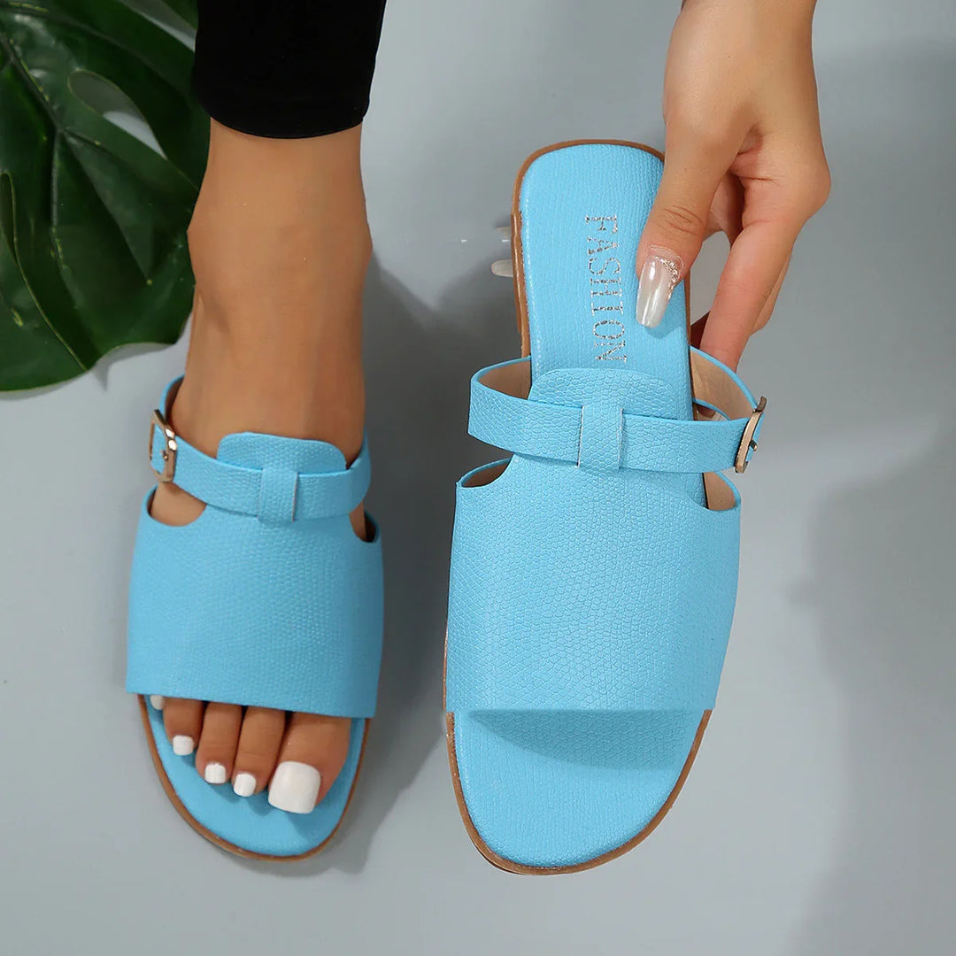 Light blue slip-on women's sandals with textured upper and buckle strap, worn on foot and held by hand