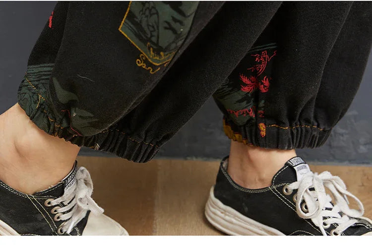 Close-up of black jogger pants with elastic cuffs and embroidered designs paired with black and white sneakers