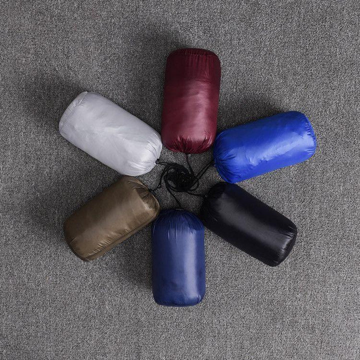 Six colorful compact sleeping bags in gray, burgundy, blue, black, navy, and brown arranged on gray carpet
