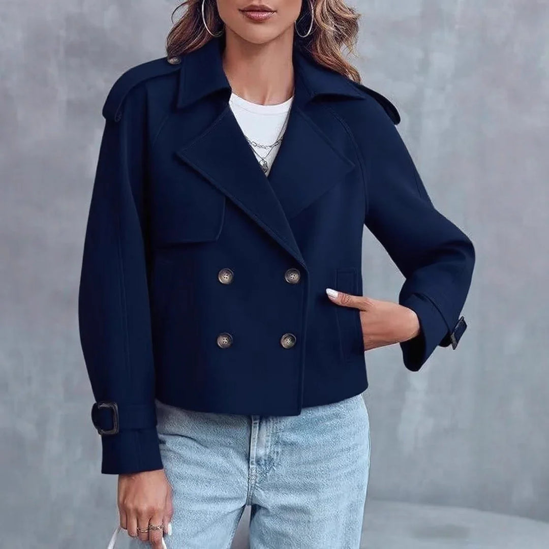 Woman wearing navy blue double-breasted cropped coat with light blue jeans and silver hoop earrings
