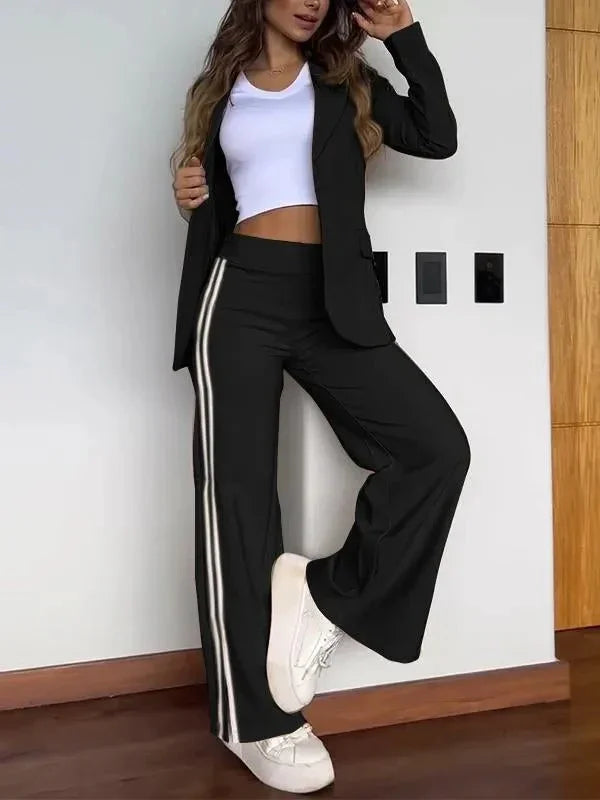 Woman wearing black blazer, white crop top, black wide-leg pants with side stripes, and white sneakers indoors
