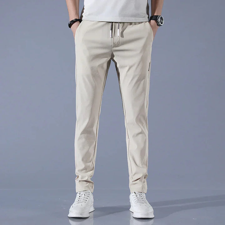 Man wearing beige slim-fit jogger pants with white sneakers against gray background