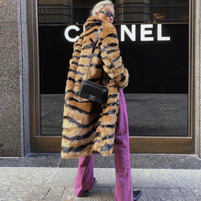 Woman in tiger-striped fur coat and purple pants standing in front of a Chanel store window