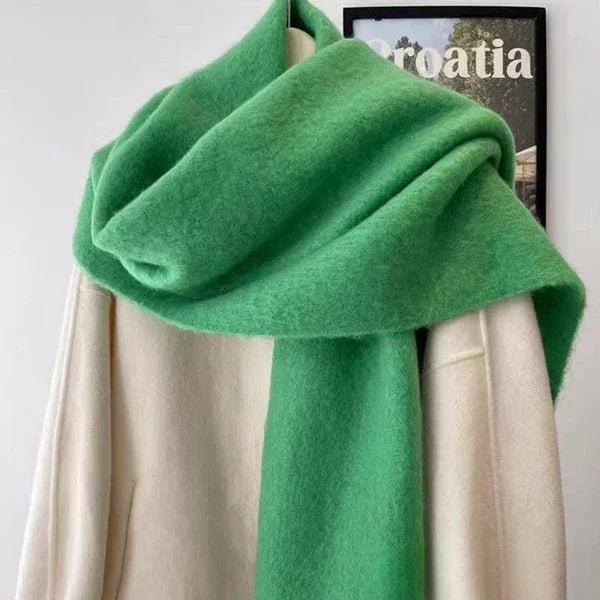 Soft green wool scarf draped over beige coat on hanger with Croatia poster background