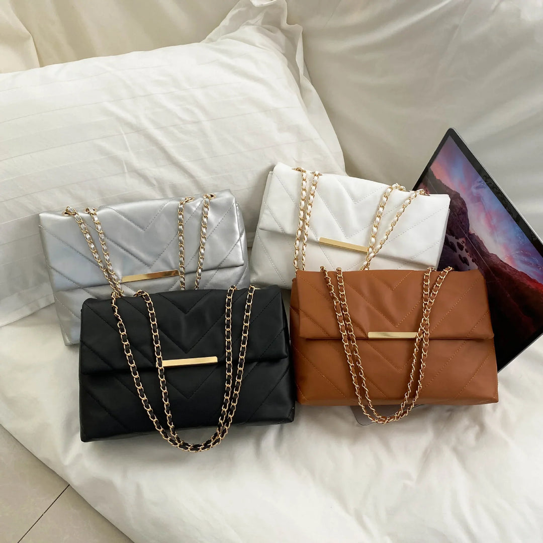 Four quilted leather chain strap handbags in silver, white, black, and brown on a white bed