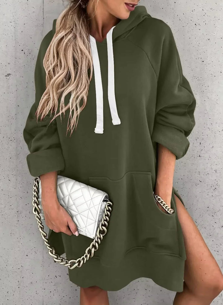 Woman wearing olive green hoodie dress with white drawstrings and holding white quilted purse with gold chain
