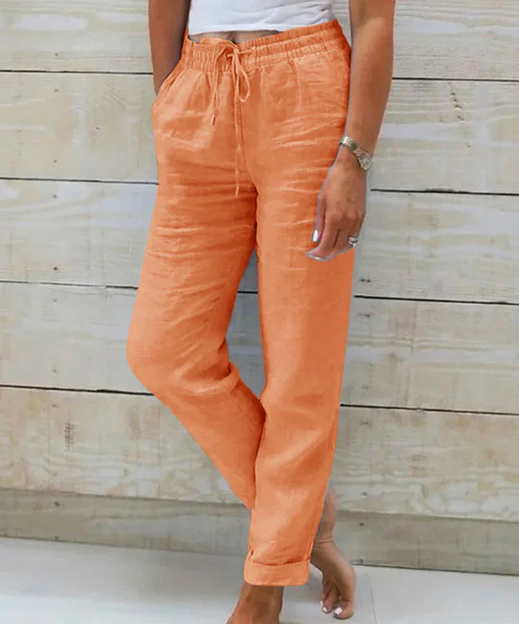 Woman wearing relaxed fit orange linen pants with drawstring waist standing barefoot against wooden wall