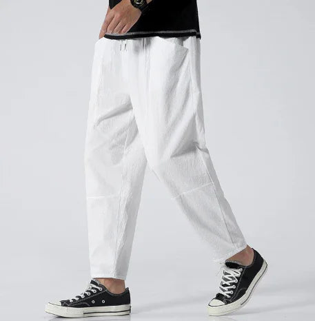 man wearing white loose-fit pants and black sneakers on gray background, casual streetwear style