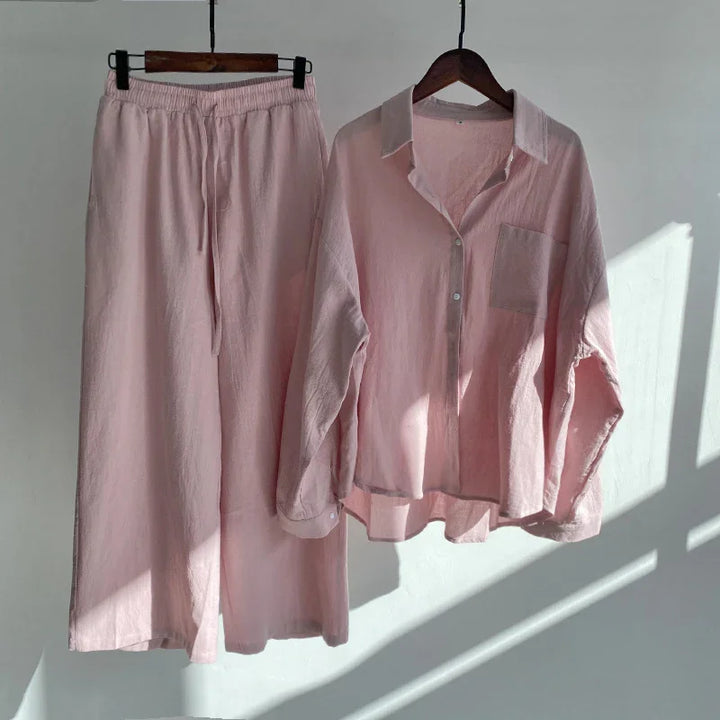 Light pink linen pajama set with button-up shirt and elastic waist pants hanging on wooden hangers