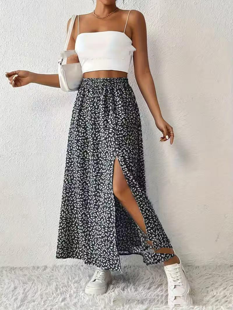Woman wearing white crop top, black floral slit maxi skirt, white sneakers, and white shoulder bag