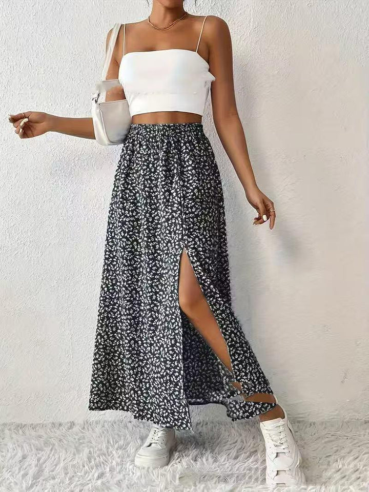 Woman wearing white crop top, black floral slit maxi skirt, white sneakers, and white shoulder bag
