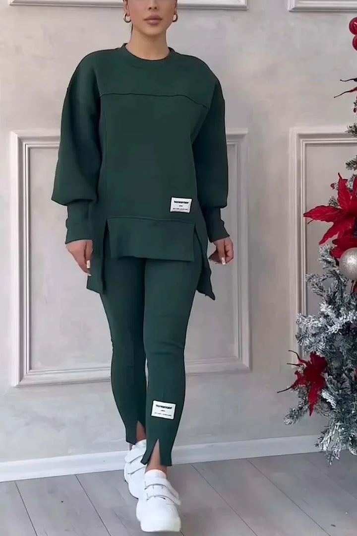 Woman wearing dark green oversized sweatshirt and matching leggings with white sneakers near Christmas decorations