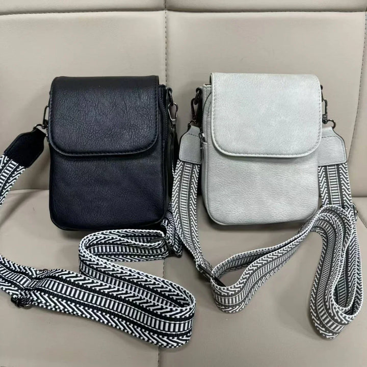 Two small leather crossbody bags in black and white with black and white patterned straps on beige surface