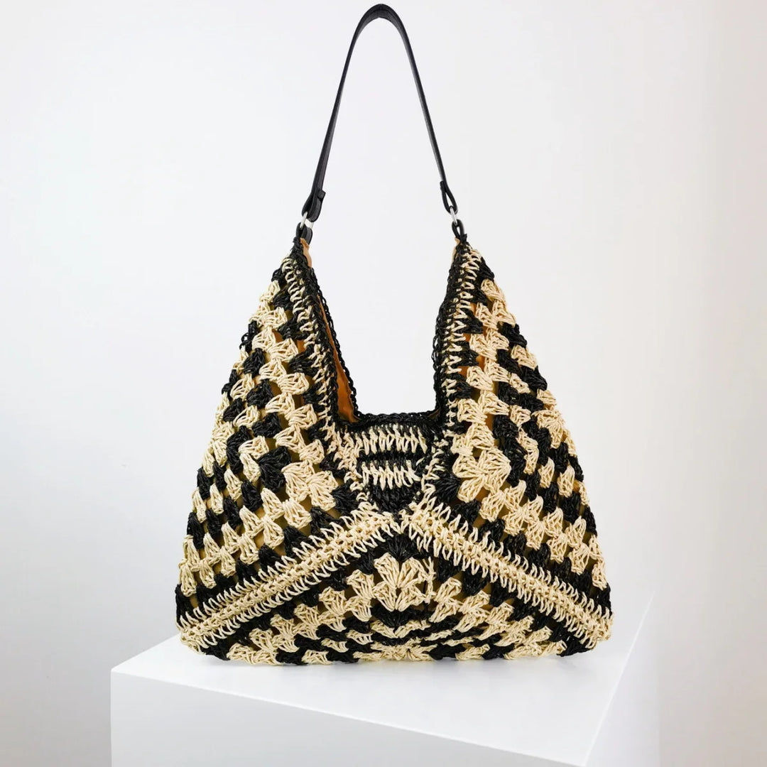 Handmade black and beige crocheted shoulder bag with leather strap on white pedestal