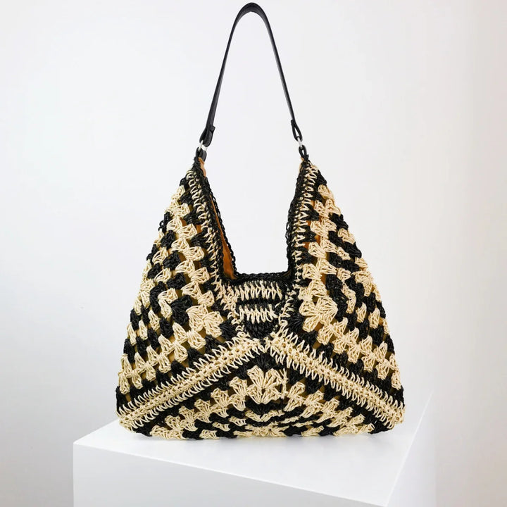 Handmade black and beige crocheted shoulder bag with leather strap on white pedestal