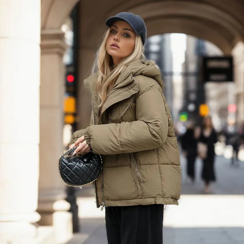 Blonde woman wearing a beige puffer jacket and black cap holding a black quilted handbag in city street