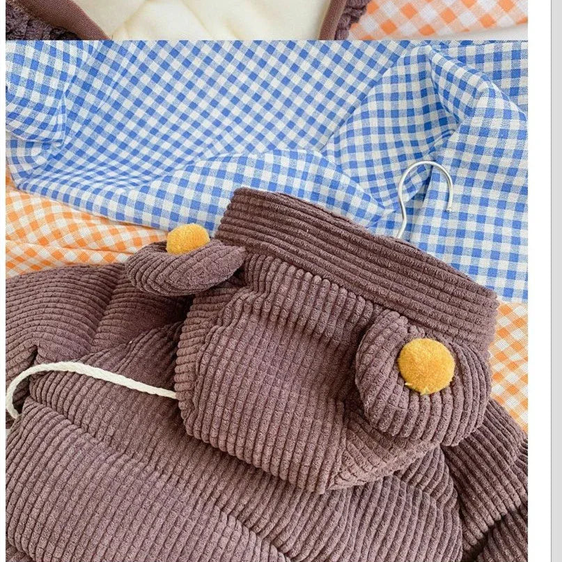 Brown corduroy baby romper with bear ears and yellow pom-poms on blue and orange checkered fabric