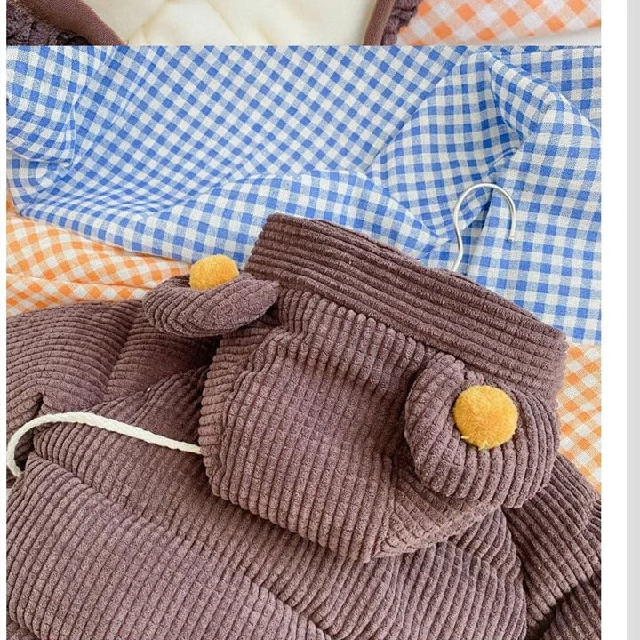 Brown corduroy baby romper with bear ears and yellow pom-poms on blue and orange checkered fabric