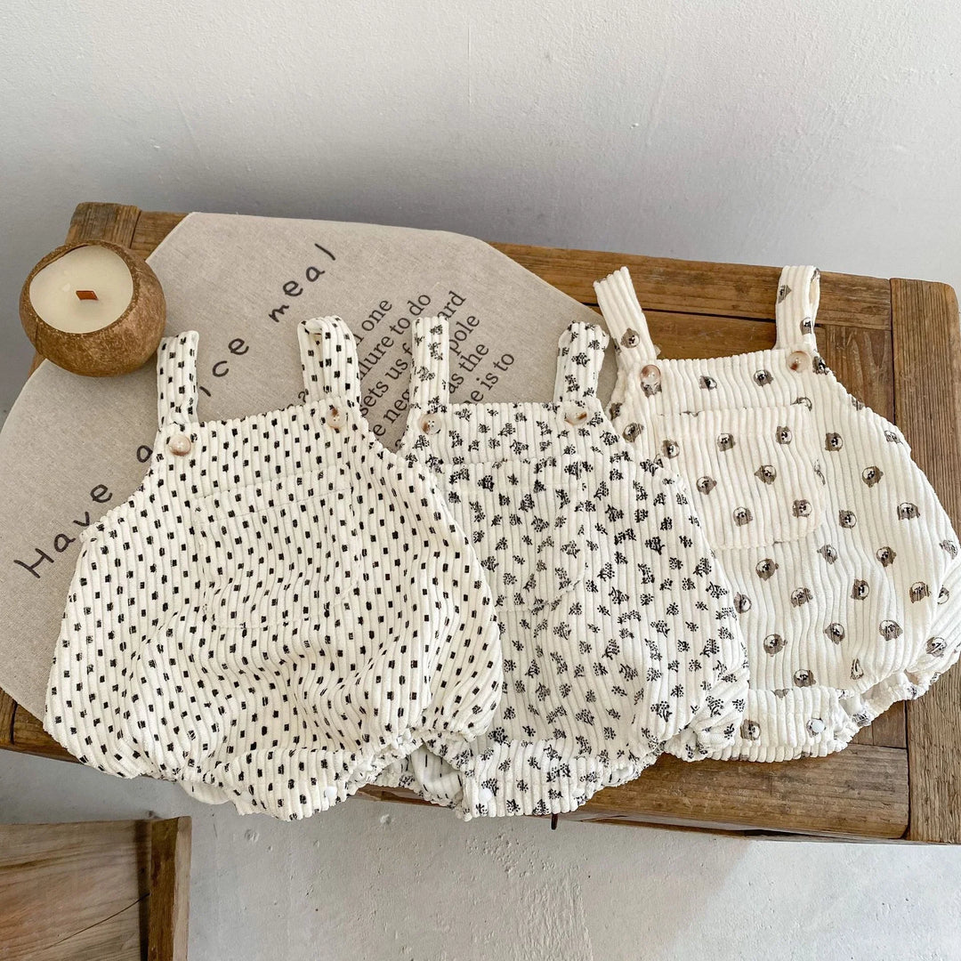 Three white baby rompers with black and brown polka dot patterns on a wooden table with decorative cloth and candle