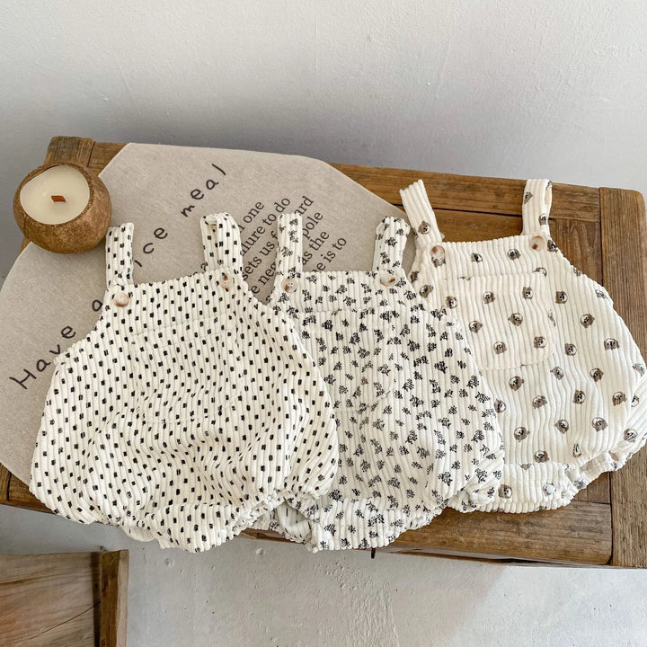 Three white baby rompers with black and brown polka dot patterns on a wooden table with decorative cloth and candle