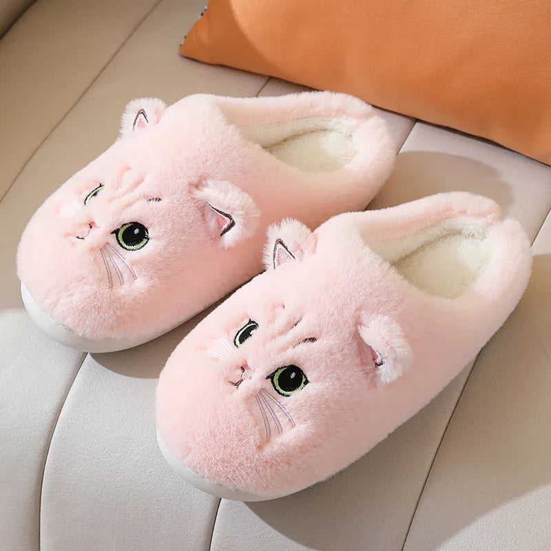 Soft pink plush slippers with cute cat faces and ears on a beige surface
