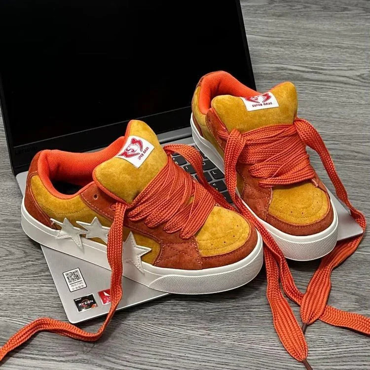 Orange and yellow suede sneakers with star accents and thick orange laces on a laptop keyboard
