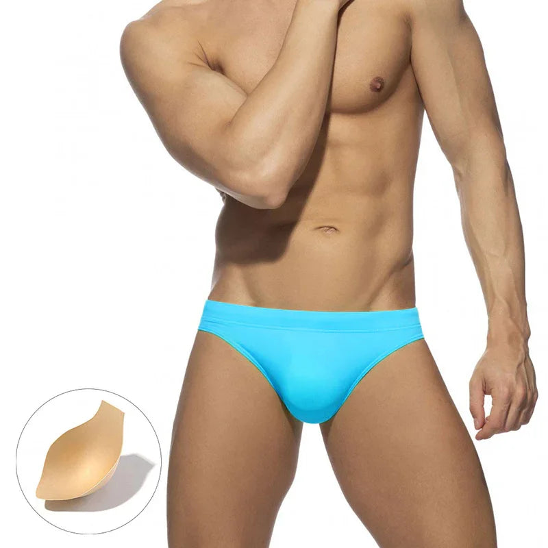 male model wearing bright blue men's swim briefs with removable padding on white background