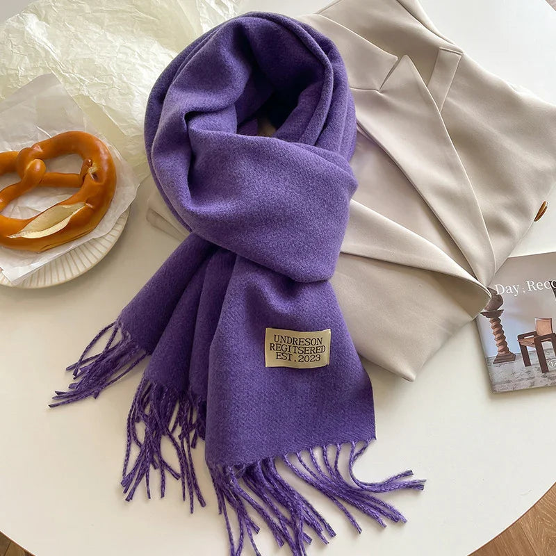 Purple fringed scarf labeled Undreson Registered Est. 2023 on beige blazer with pretzel on white plate