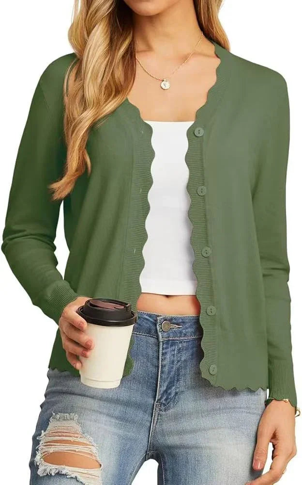 Woman wearing green scalloped-edge buttoned cardigan over white crop top and ripped blue jeans, holding coffee cup