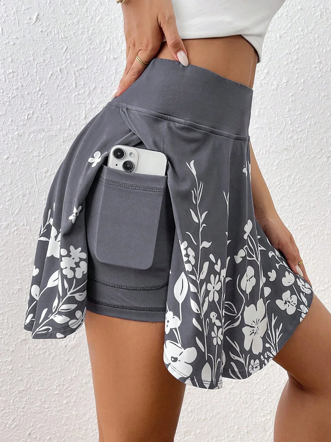 Woman wearing grey floral print skort with phone pocket holding a smartphone, close-up side view