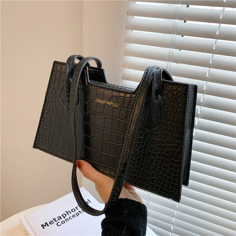 Hand holding black crocodile texture JINGPINJIU handbag near window blinds and book
