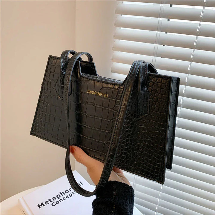 Hand holding black crocodile texture JINGPINJIU handbag near window blinds and book
