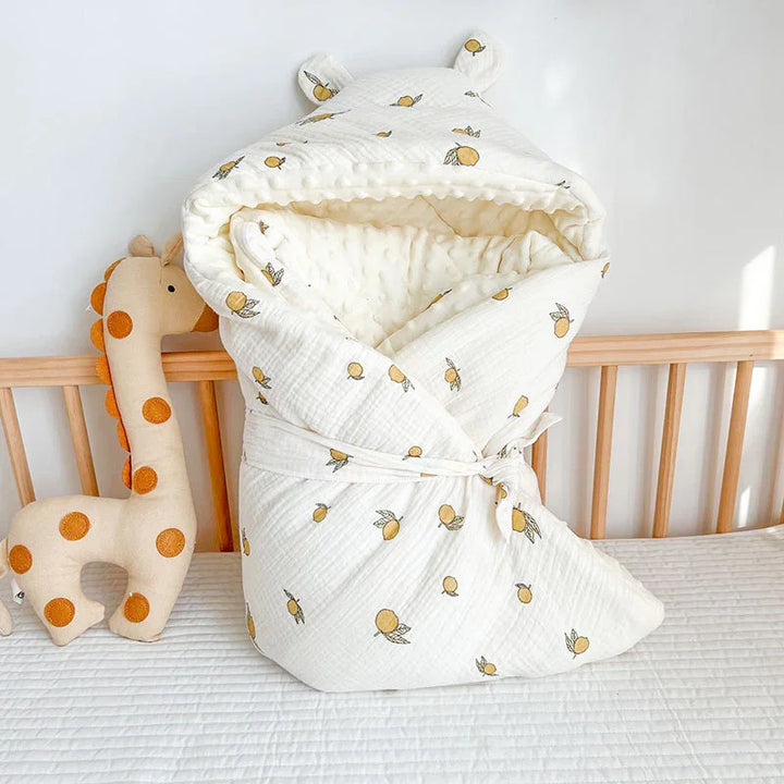 White baby swaddle blanket with yellow fruit pattern and bear ears on wooden crib with giraffe plush