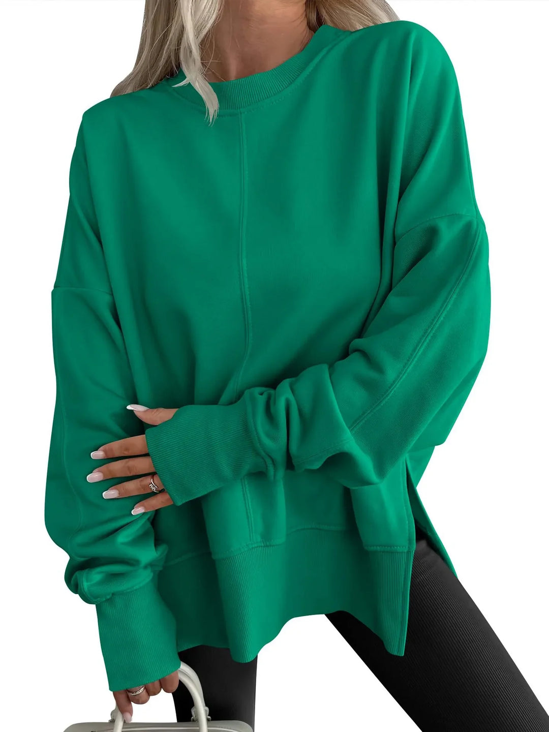 Woman wearing oversized green sweatshirt with ribbed cuffs and black leggings holding white bag